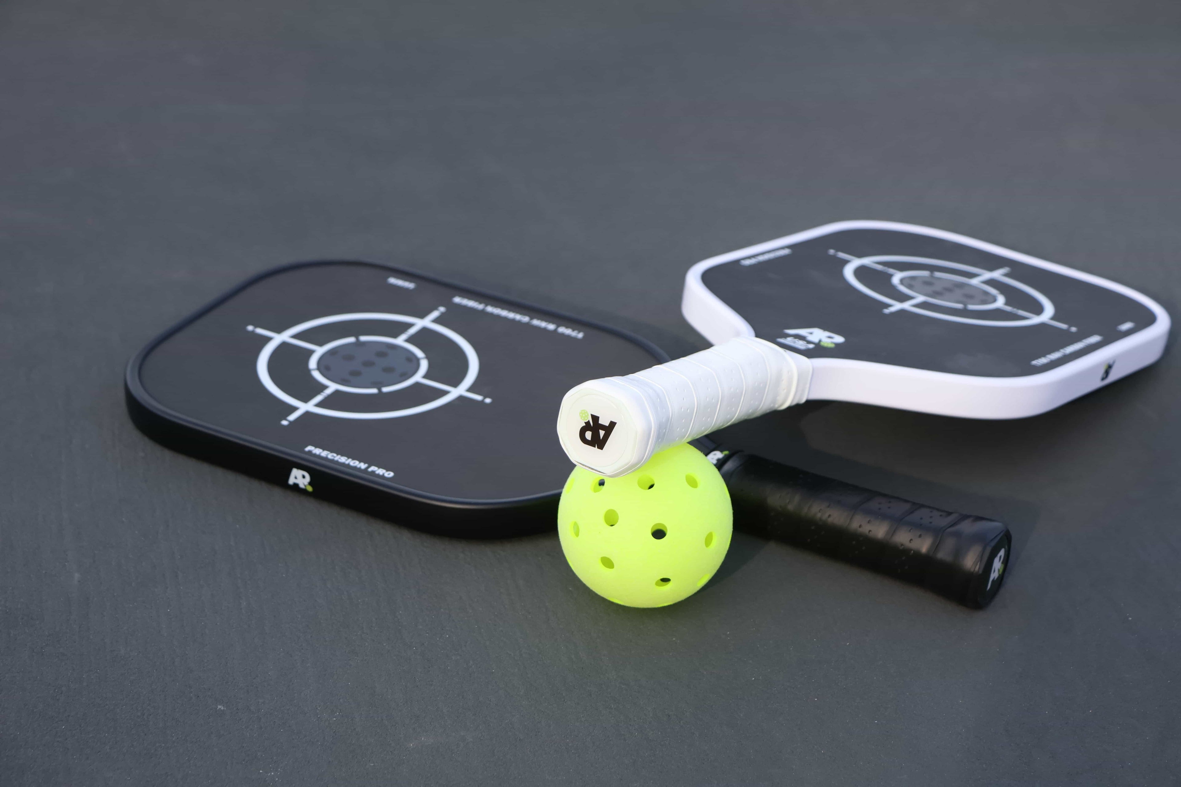 Two pickleball paddles with a green ball on a dark surface