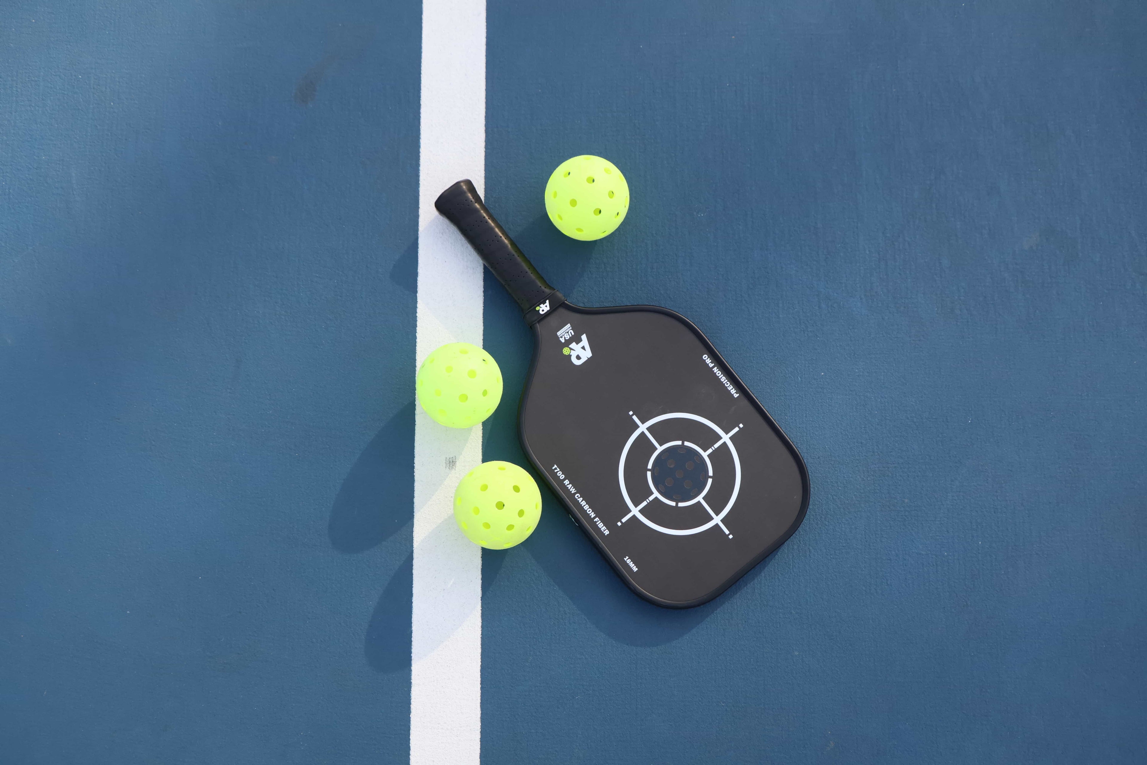 Pickleball paddle with three balls on a blue court