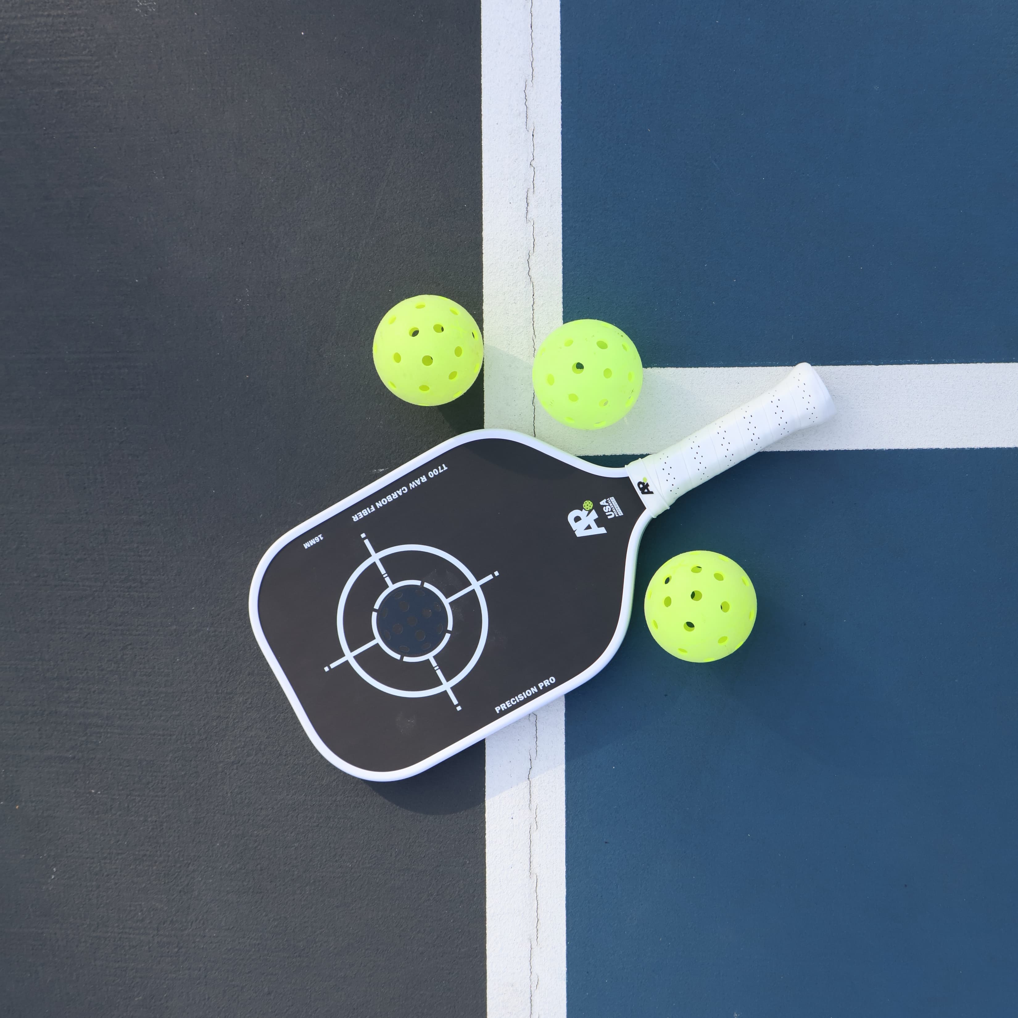 Pickleball paddle with three balls on a pickleball court